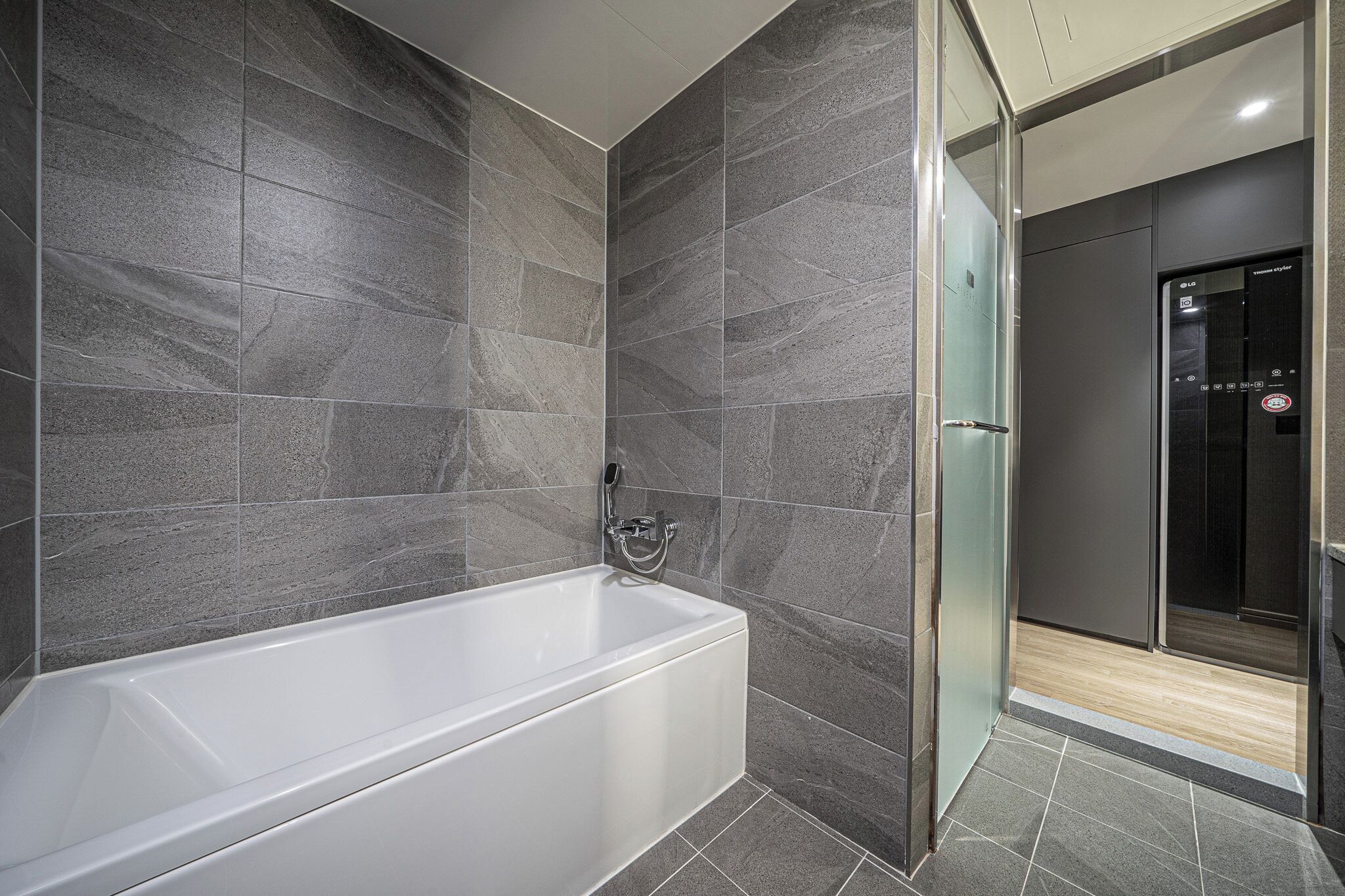 A modern bathroom with a white bathtub, dark tiled walls, and a glass shower enclosure.