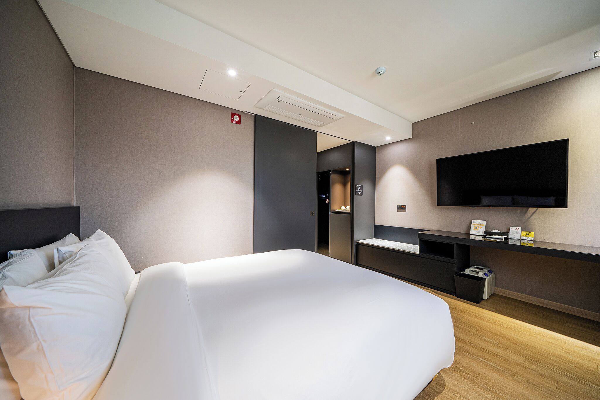 Une chambre d’hôtel moderne dotée d’un grand lit, d’un téléviseur à écran plat fixé au mur, d’un bureau avec un ordinateur et d’une petite poubelle.