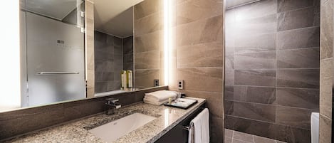 A modern bathroom with a large mirror, a granite countertop, a sink, and a shower area.