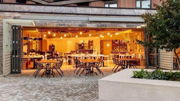 An outdoor café with tables and chairs, a stone wall, and a tree. - Vienna House Kronberg (Kronberg)