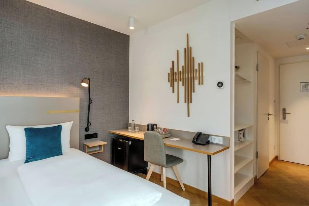 Ett hotellrum med en säng, ett skrivbord, en stol och en dekorativ väggdekoration.