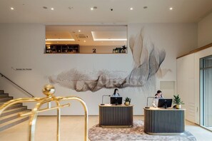Un área de recepción moderna con un gran cuadro abstracto en la pared, dos mostradores de recepción y una escalera con barandales dorados.