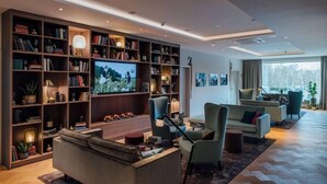 A modern living room with a large TV, bookshelves, and comfortable seating. - Vienna House Kronberg (Kronberg)