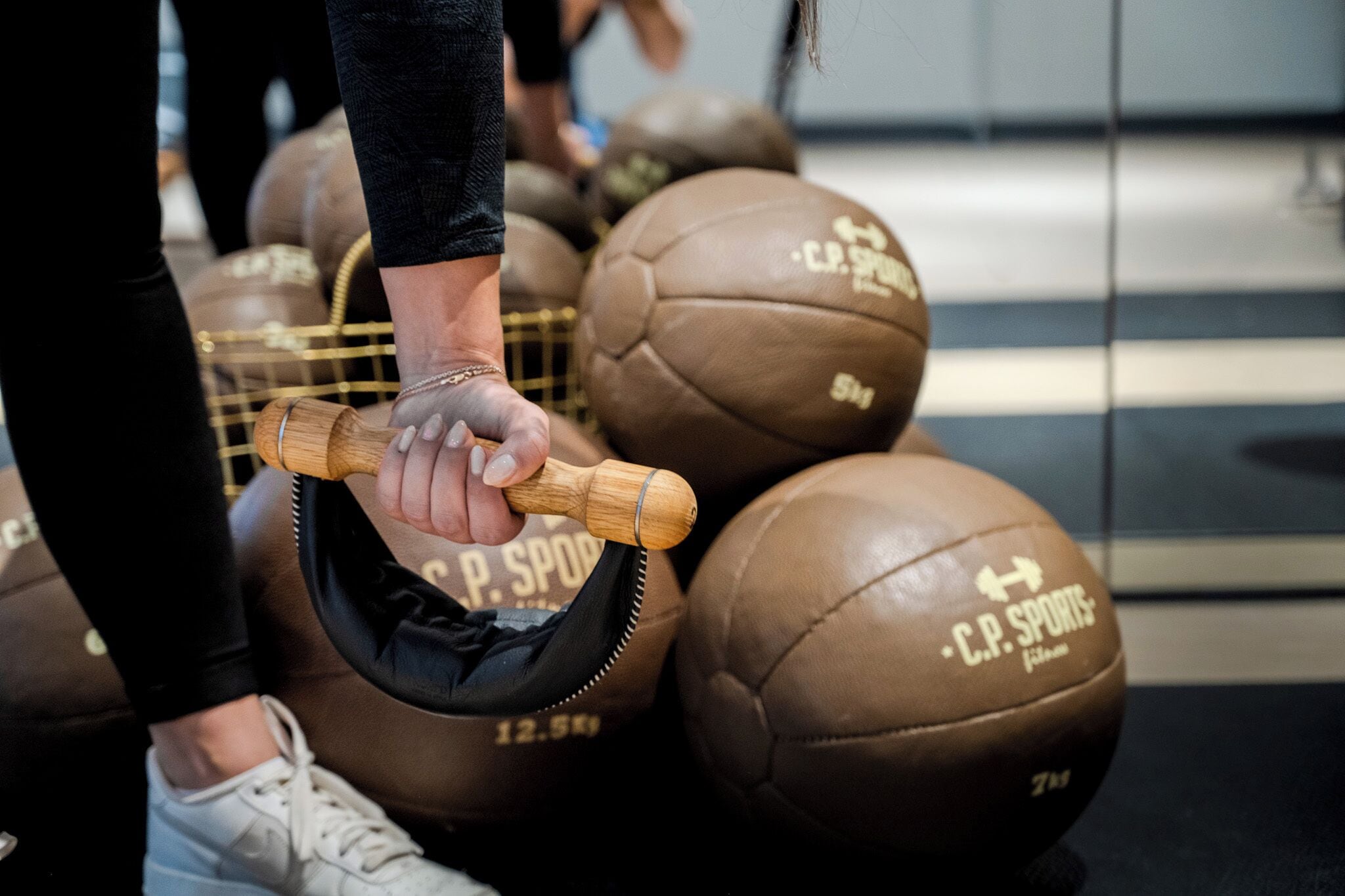 Gros plan d’une main tenant un haltère à manche en bois, muni d’un disque de poids noir portant l’inscription « C.P. SPORTS ».