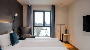 A modern hotel room with a large bed, a chair, a desk, and a TV.
