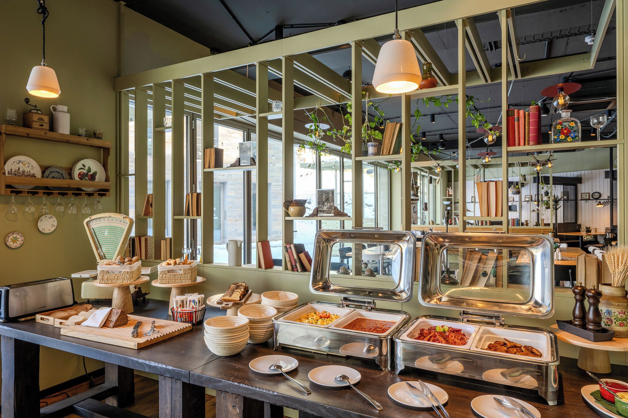 A buffet setup with various food items, a counter with plates and utensils, and shelves with kitchenware.