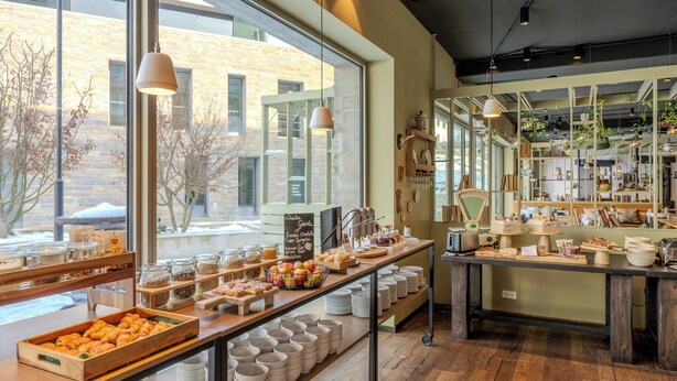 Un café doté d’une grande fenêtre, de tables en bois et où divers plats sont exposés.