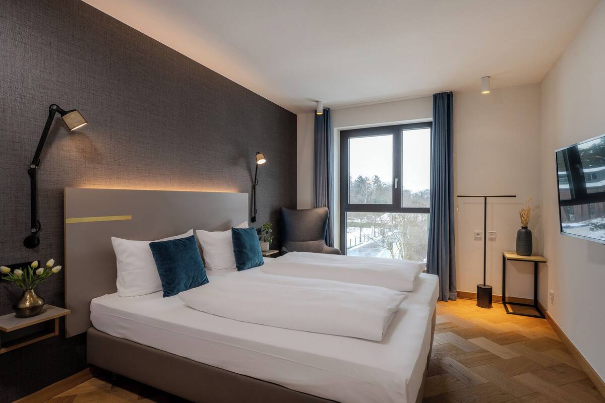 Une chambre d’hôtel moderne dotée d’un grand lit, de lampes de chevet, d’un téléviseur à écran plat et offrant une vue sur l’extérieur.