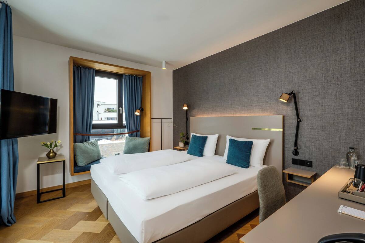 Une chambre d’hôtel avec un grand lit, un bureau, une télévision et une fenêtre avec des rideaux.