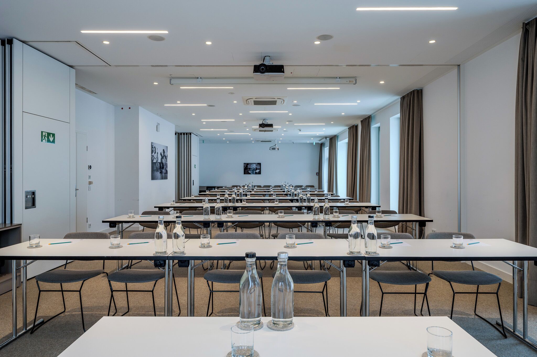Una sala de conferencias con varias mesas, sillas y una pantalla para proyector.