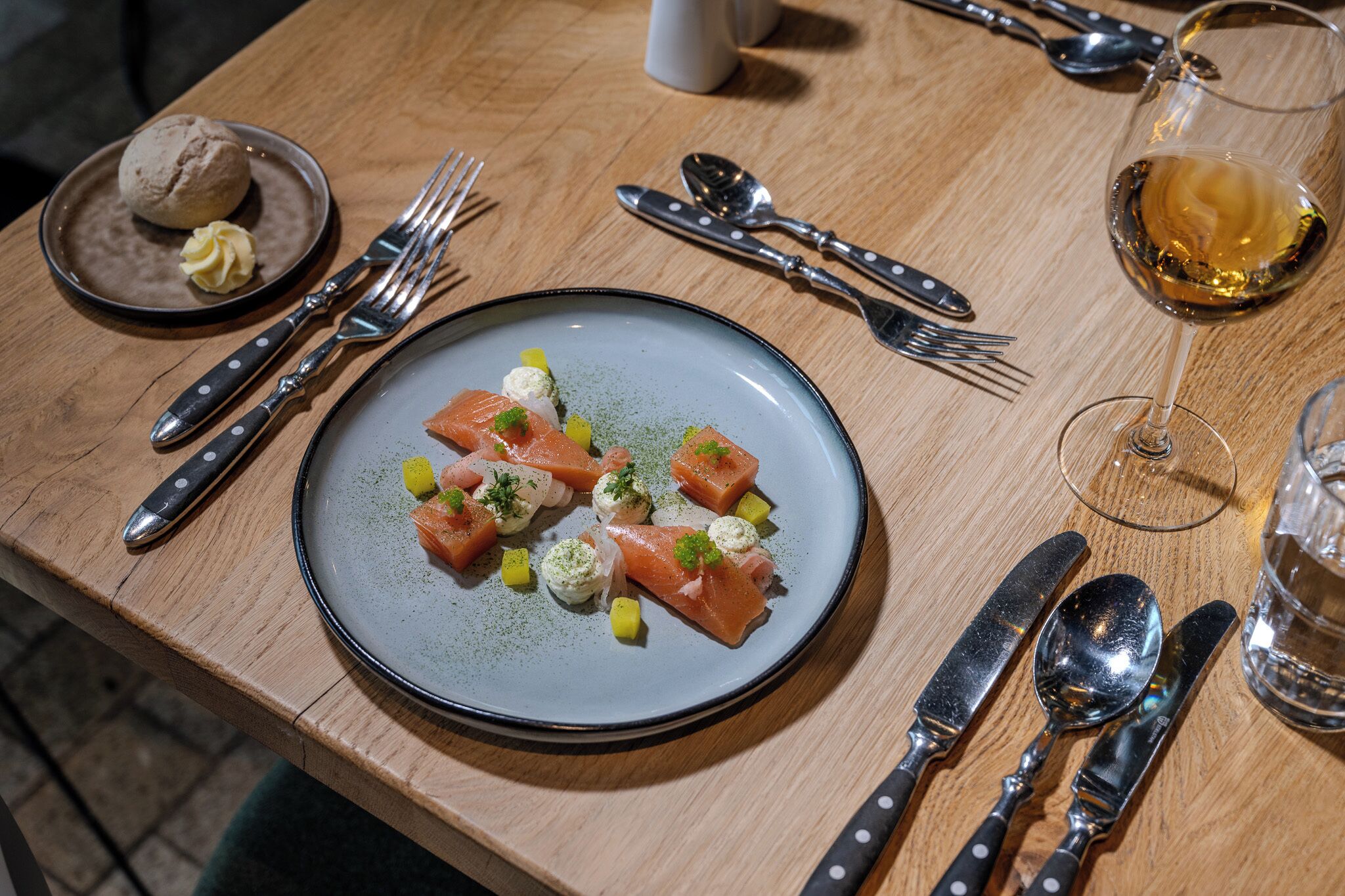 A dining table with a plate of salmon, utensils, and a glass of wine.