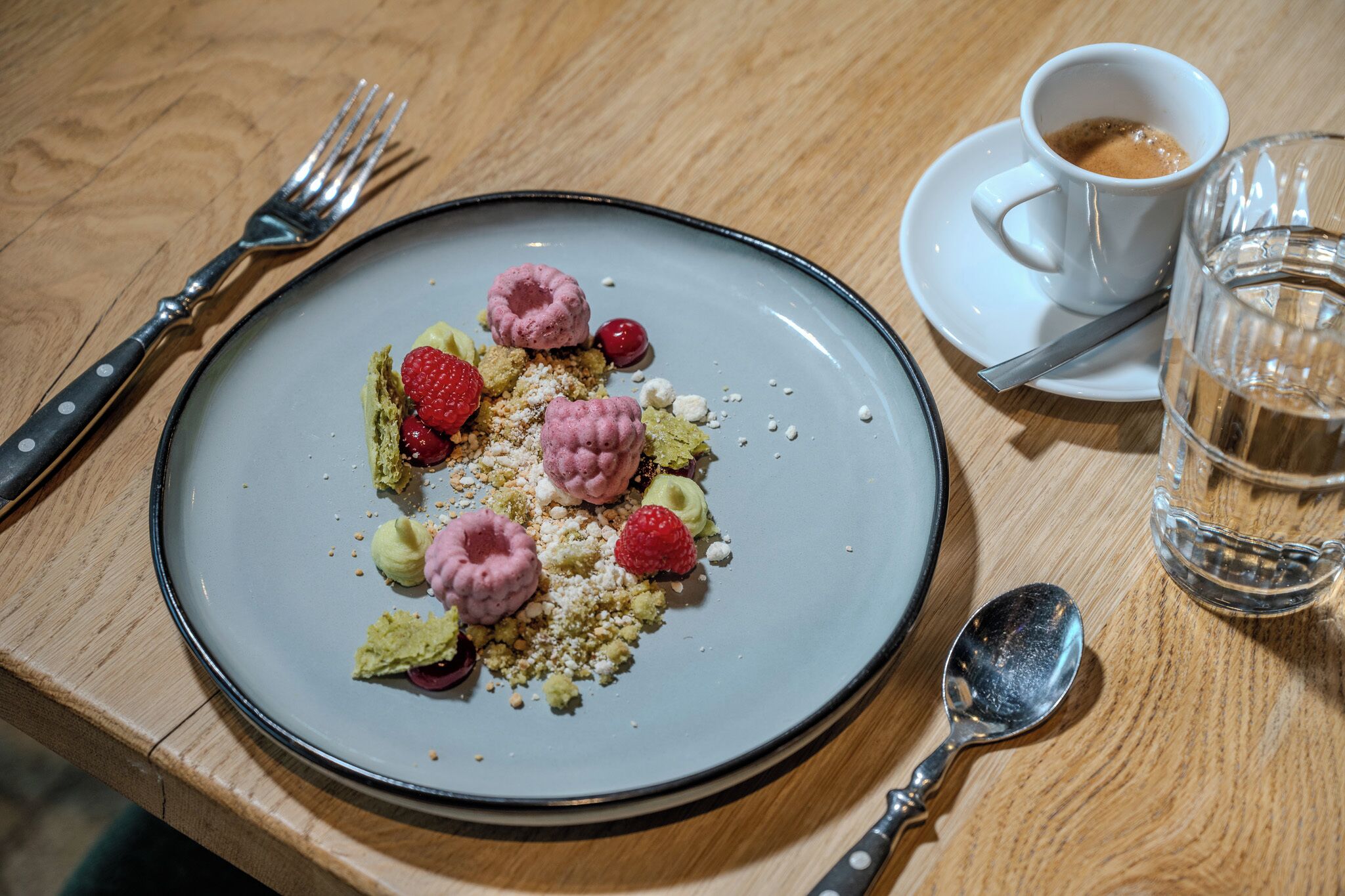 Een bord dessert met frambozen en meringues op een houten tafel.