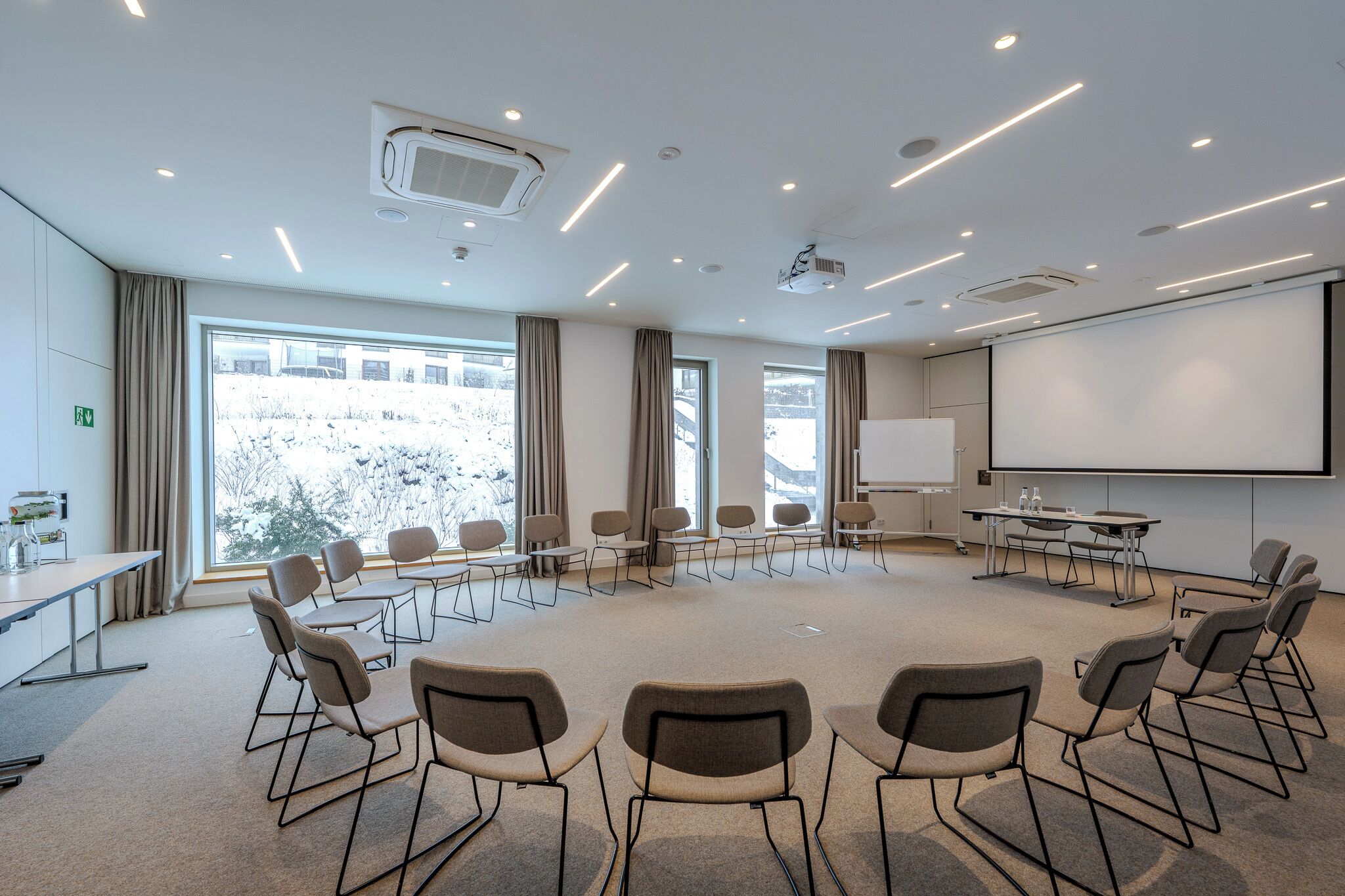A conference room with a large screen, multiple tables, and chairs arranged in a semi-circle.