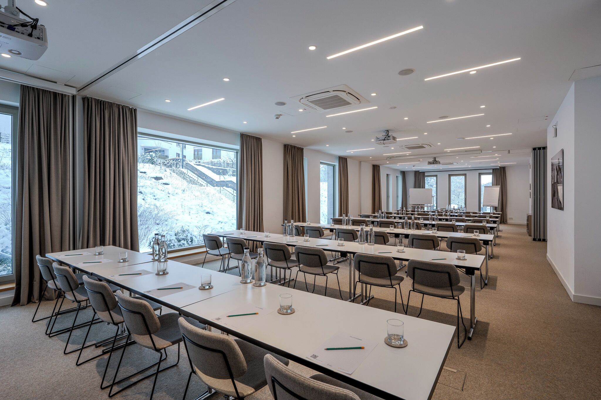 A conference room with long tables, chairs, and a projector screen.