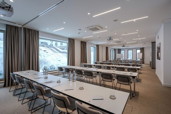 A conference room with long tables, chairs, and a projector screen.