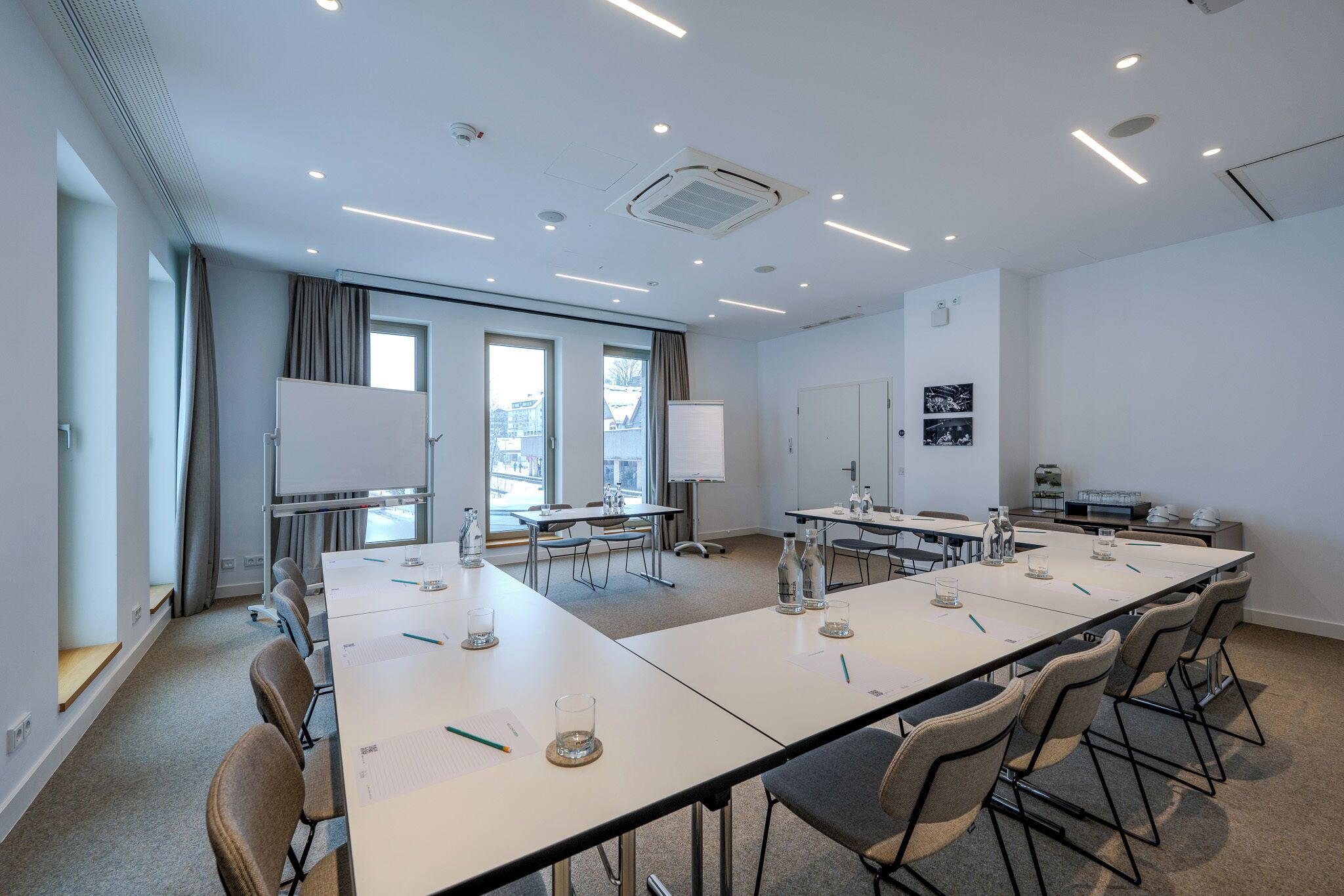 Une salle de conférence avec une longue table, des chaises, un tableau blanc et une fenêtre avec des rideaux.