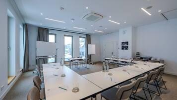 Une salle de conférence avec une longue table, des chaises, un tableau blanc et une fenêtre avec des rideaux.