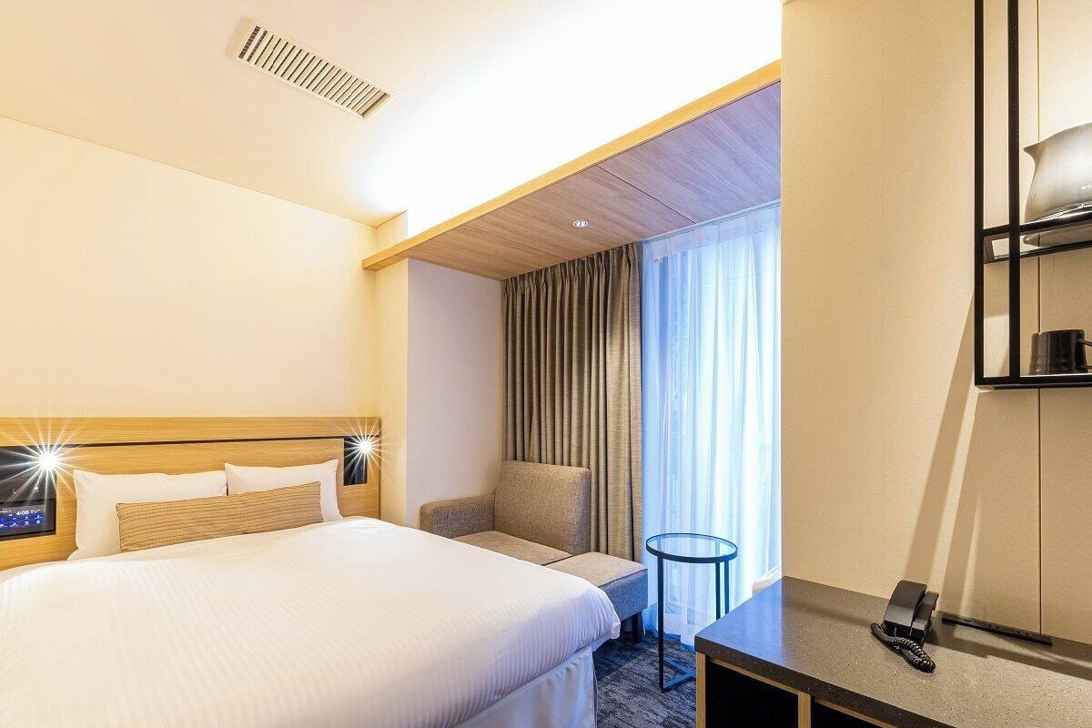 A hotel room with a large bed, a small sofa, a desk with a telephone, and a window with curtains.