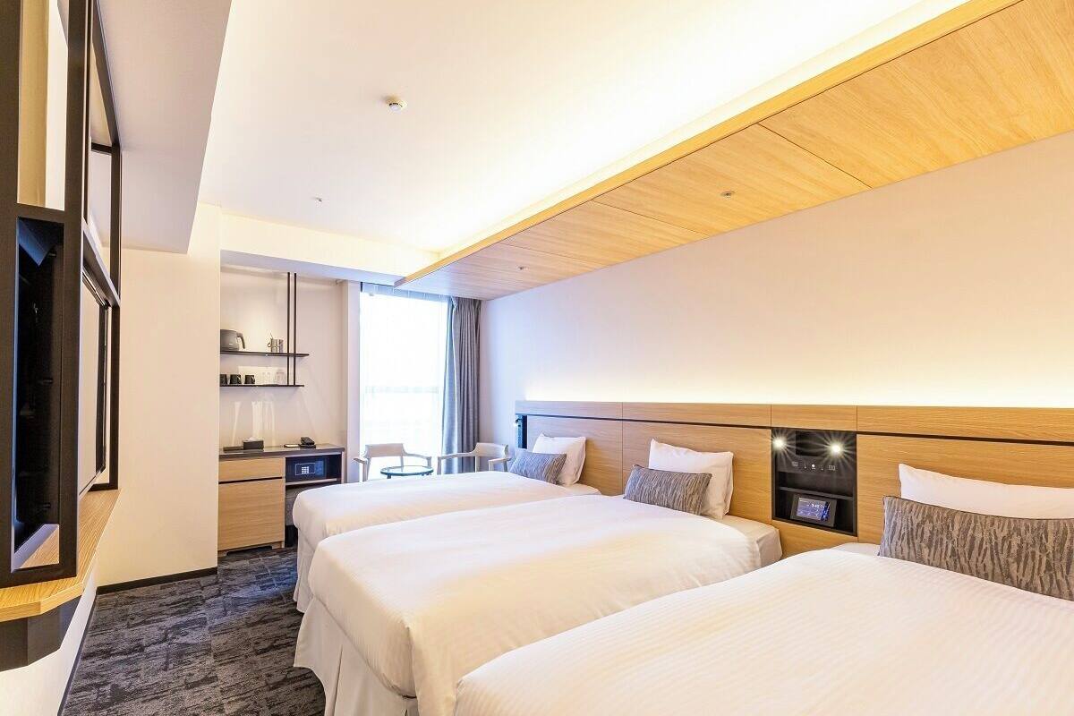 A hotel room with two beds, a desk, a chair, and a TV.