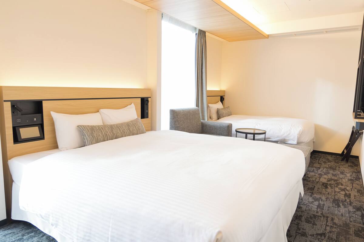 A hotel room with a large bed, a smaller bed, a chair, and a small table.