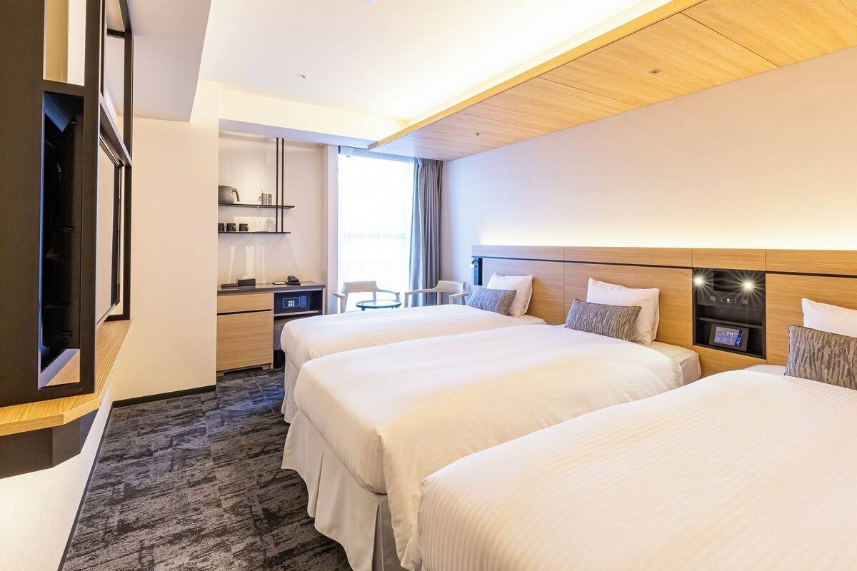 A hotel room with two beds, a desk, a chair, and a TV.
