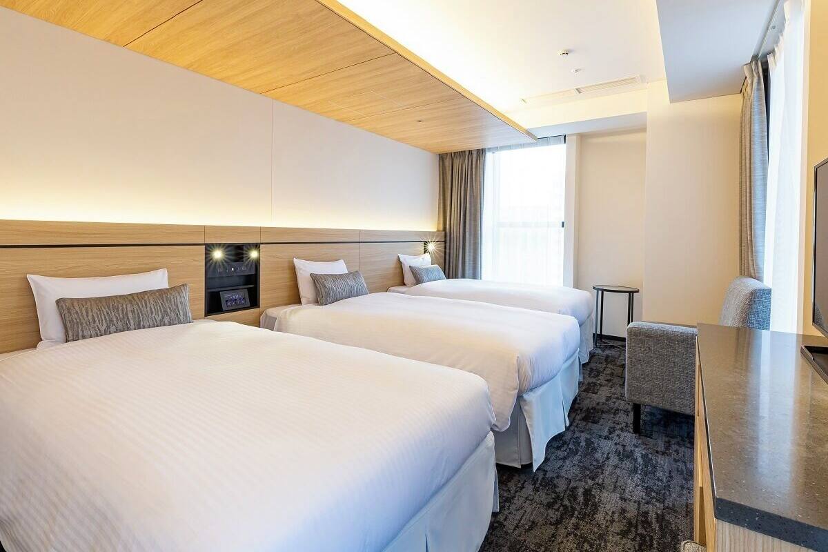 A hotel room with three beds, a desk, and a television.