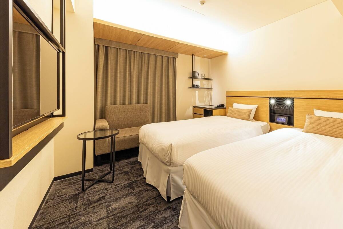 A hotel room with two beds, a small table, a sofa, and a TV.