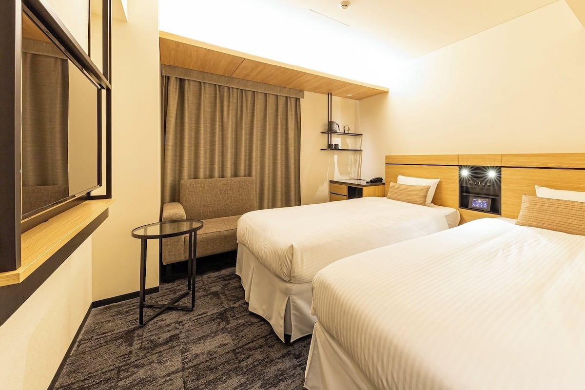 A hotel room with two beds, a small table, a sofa, and a TV.