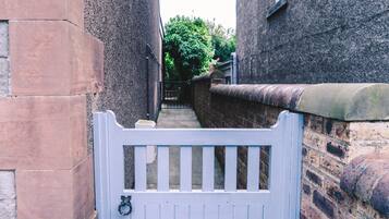 A narrow alleyway with a white gate, brick walls, and a stone wall with a metal gate.