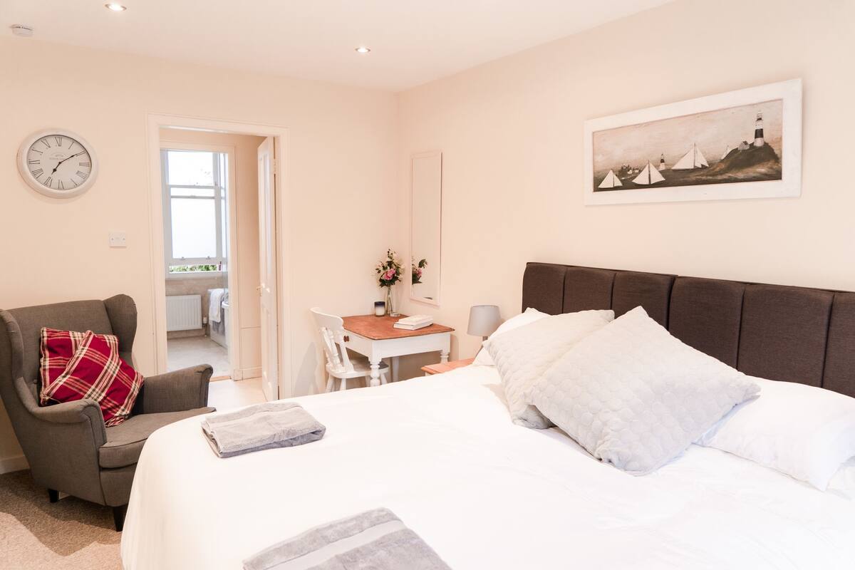 A bedroom with a large bed, a chair, a desk, and a painting on the wall.