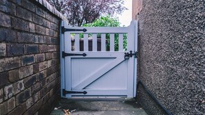 A white metal gate with a diagonal latch, set in a brick wall with a concrete base. - A Stay On The Brae (Edinburgh)