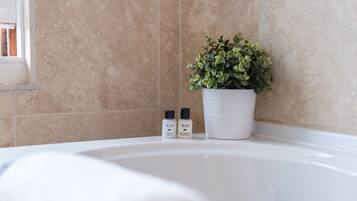 A bathroom with a bathtub, a potted plant, and two bottles of shampoo.