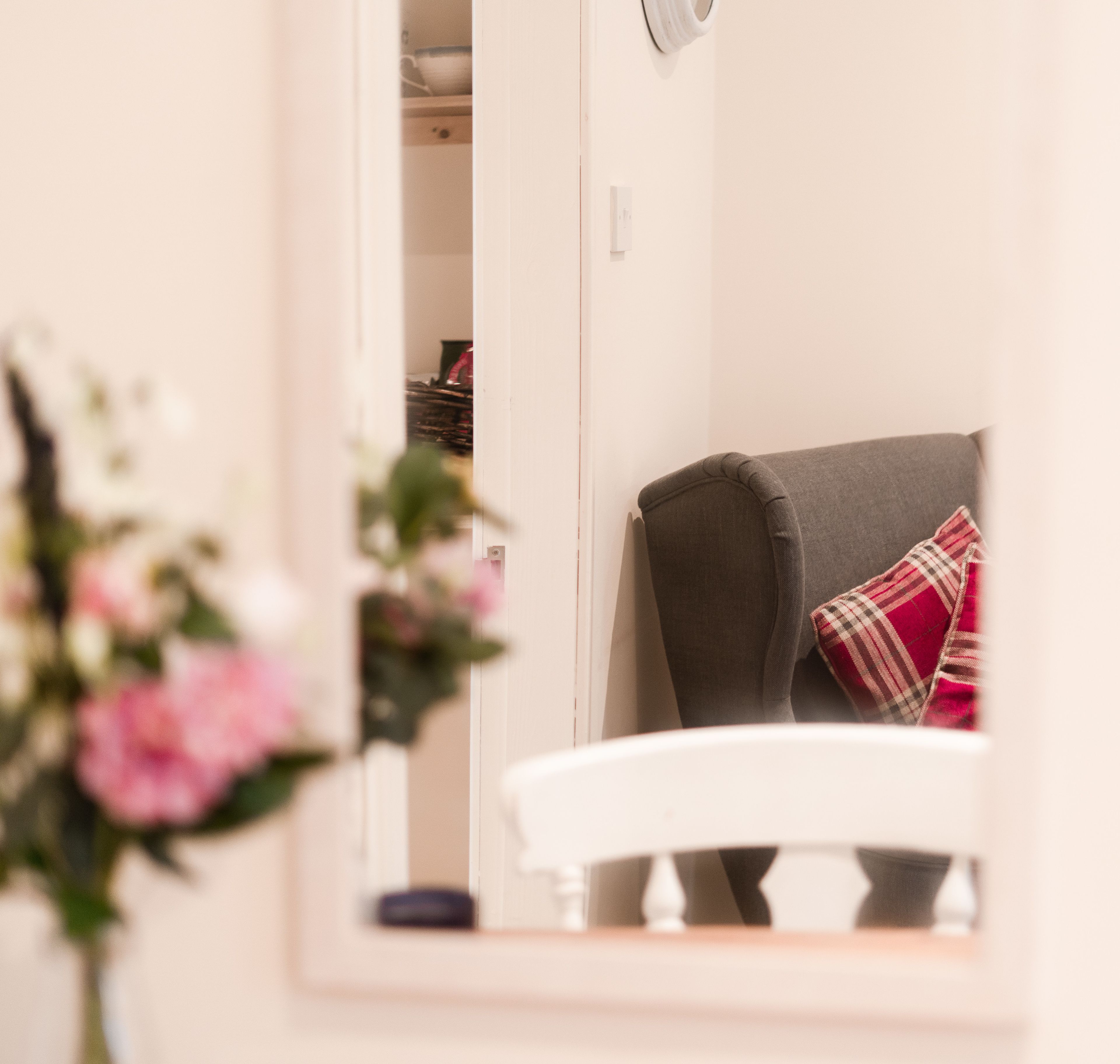 A room with a white chair, a grey sofa with a plaid pillow, and a white wall.