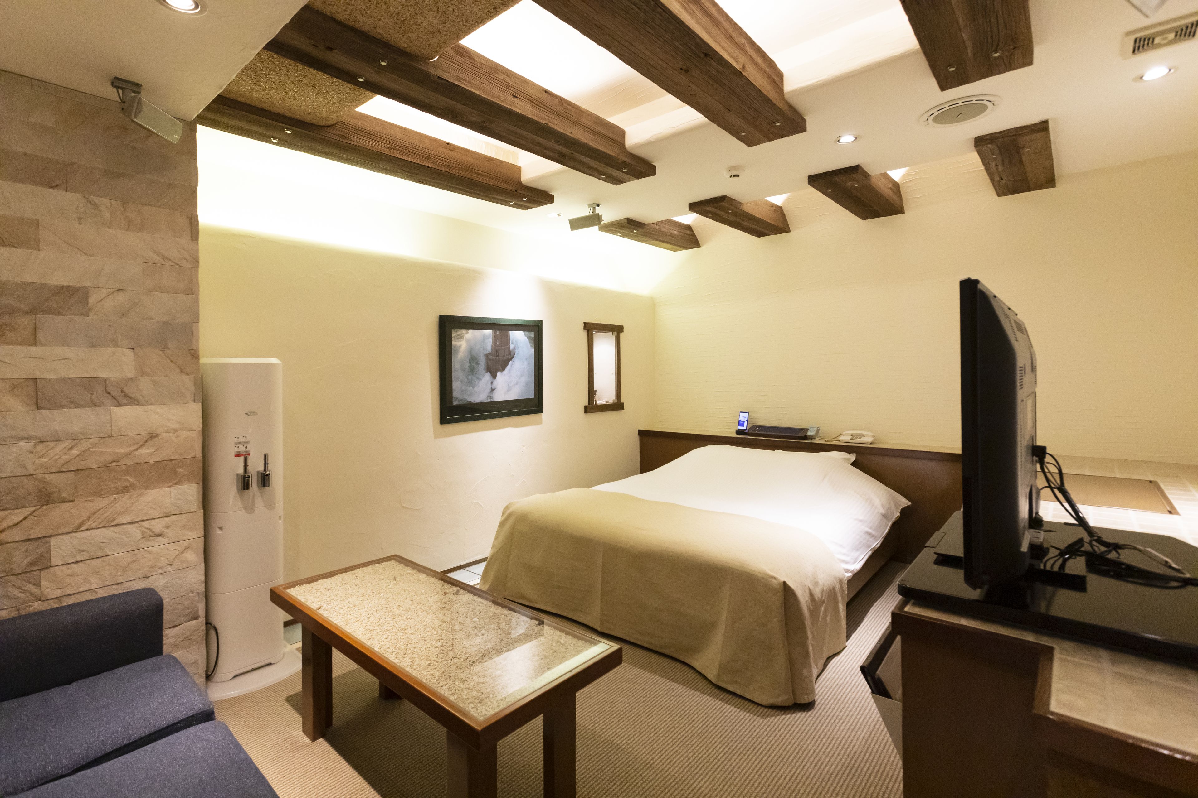 A hotel room with a bed, a television, a small table, and a stone wall.