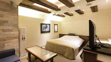 A hotel room with a bed, a television, a small table, and a stone wall.