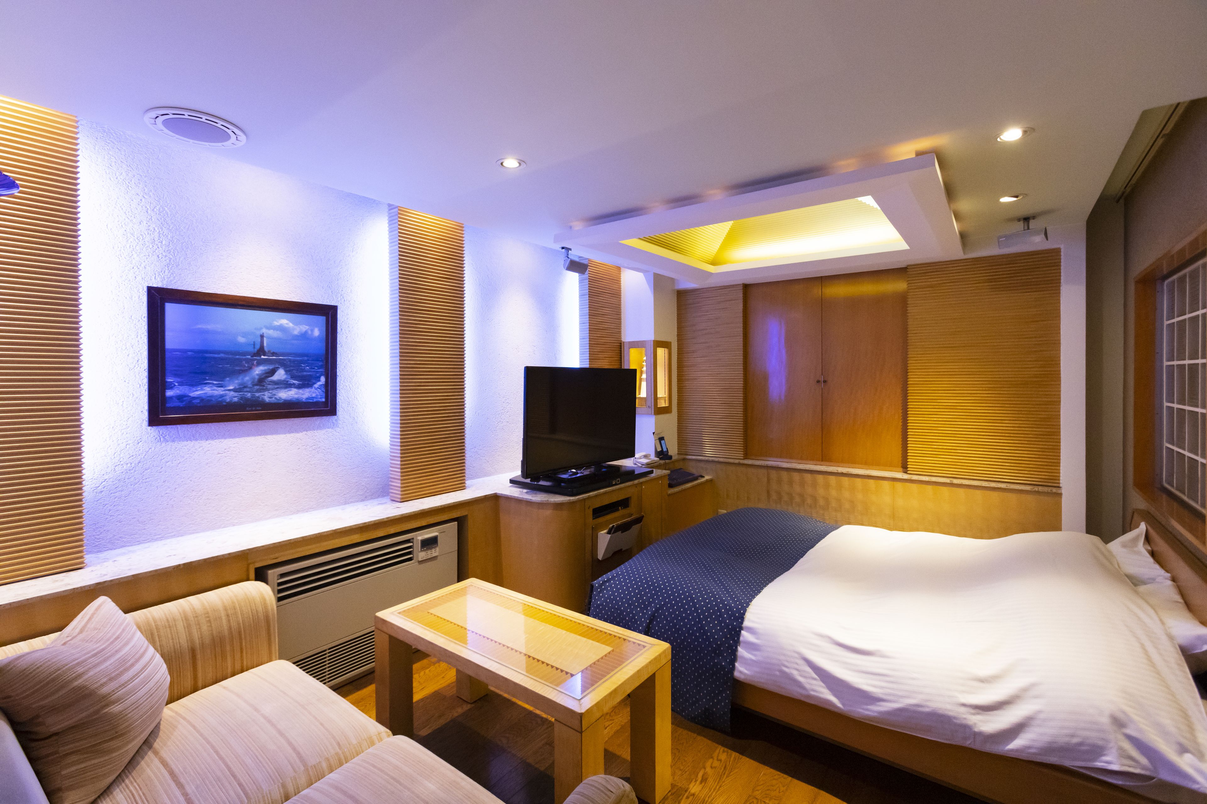 A hotel room with a bed, a TV, a desk, and a sofa.