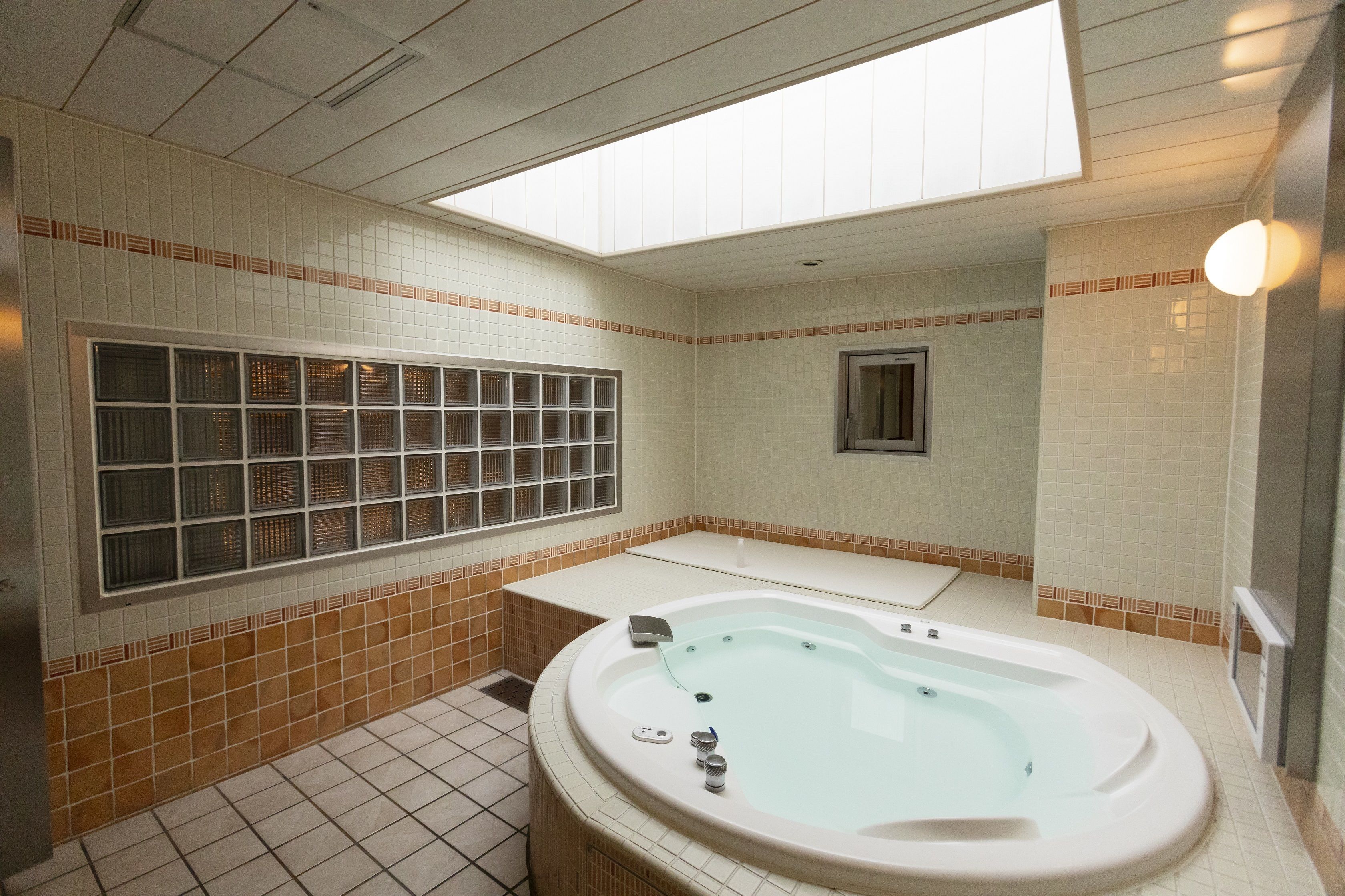 Een badkamer met een groot raam, een bad, een douche en een betegelde vloer.