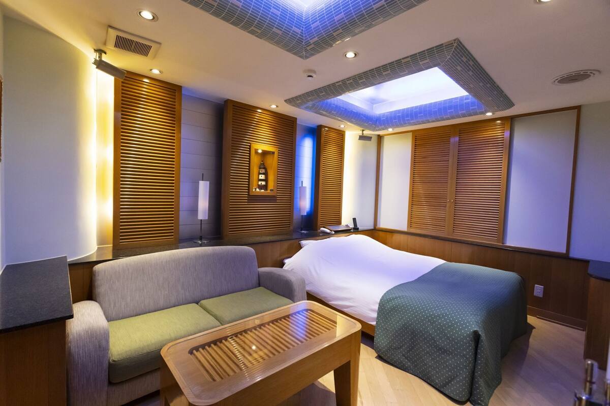 A hotel room with a bed, a sofa, a small table, and a ceiling light fixture.