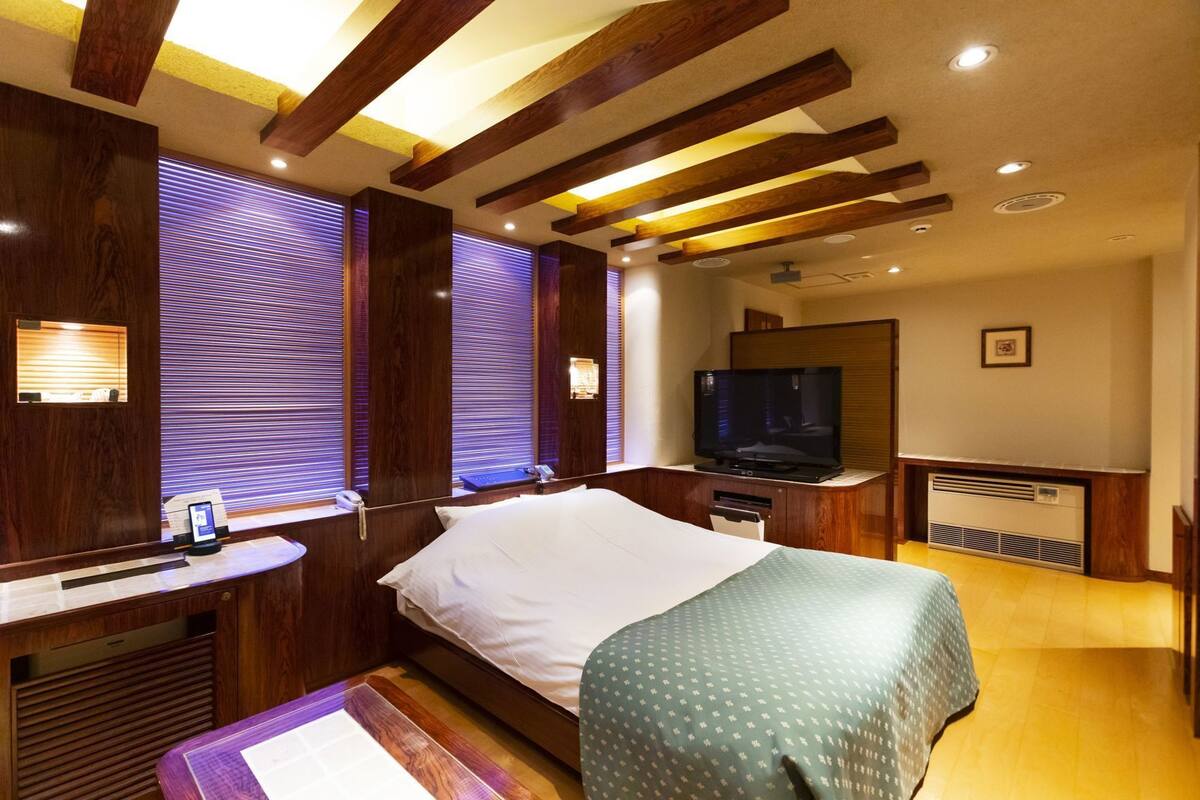 A hotel room with a bed, a television, a desk with a phone, and wooden ceiling beams.