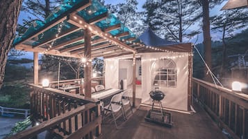 Une terrasse en bois dotée d’un espace salon couvert, de guirlandes lumineuses et d’un barbecue.