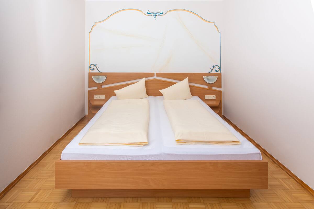 A single bed with a wooden frame and headboard, two pillows, and a white bedspread.