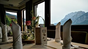 A table set for dining with a mountain view, a menu stand, and a vase with flowers. - Walter's Gästehaus (Assling)
