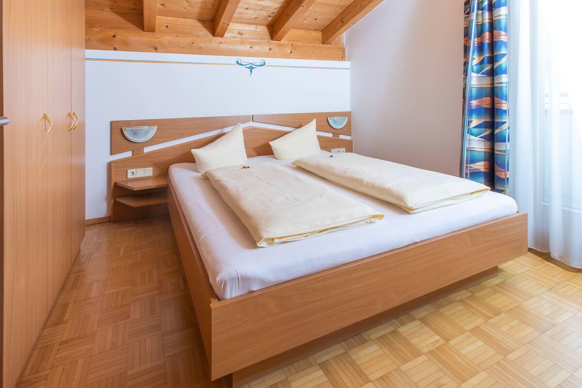 A bedroom with a wooden bed, a nightstand, and a wall-mounted shelf.
