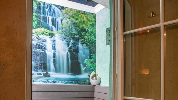 A glass door leading to a bathroom with a view of a waterfall and a bench. - Walter's Gästehaus (Assling)