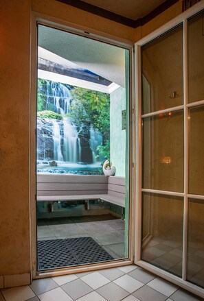 Puerta de cristal que da a un baño con vistas a una cascada y una banca.