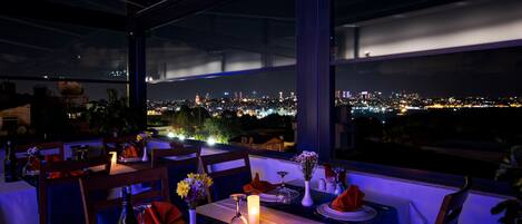 A restaurant with tables set for dining, featuring a city view at night.