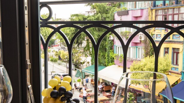 Un balcó amb un plat de fruita i un got de vi, amb vista a un carrer colorit i terrasses.