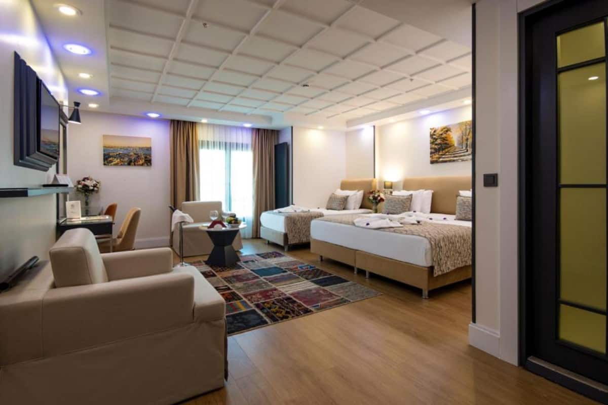 A hotel room with a large bed, two smaller beds, a sofa, a desk, and a TV.