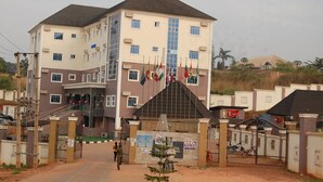 A multi-story building with a gated entrance, flags, and a staircase leading to the entrance. - Golden Valley Hotel Enugu (Nsukka)