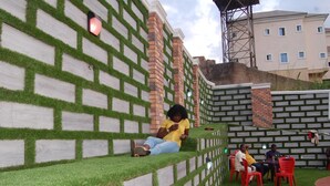 A seating area with brick and grass wall design, outdoor tables, and chairs. - Golden Valley Hotel Enugu (Nsukka)